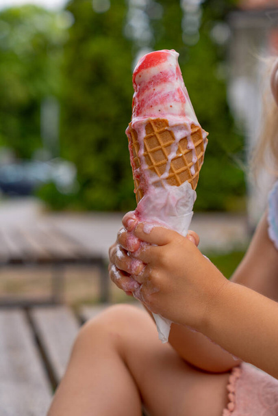 A fagylaltot egy gofris tölcsérben olvasztják el egy gyerek kezében.. - Fotó, kép