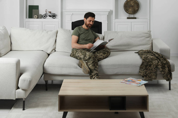 Happy soldier reading magazine on sofa in living room. Military service - Foto, Bild