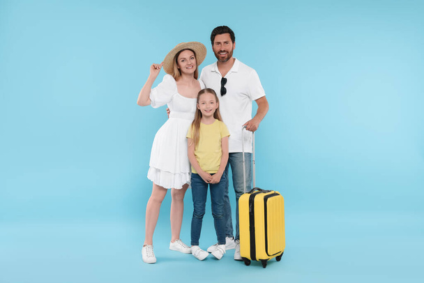 Ευτυχισμένη οικογένεια με κίτρινη βαλίτσα σε γαλάζιο φόντο - Φωτογραφία, εικόνα