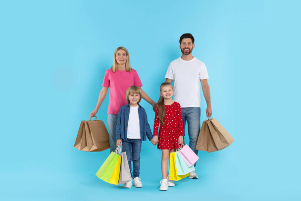 Family shopping. Happy parents and children with many colorful bags on light blue background - Photo, image