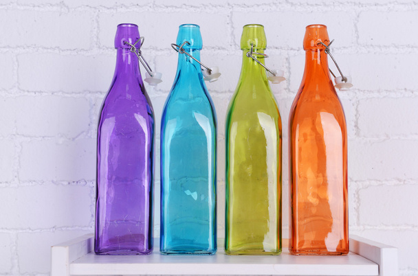 Interior design with colorful decorative glass bottles on tabletop on white brick wall background - Foto, afbeelding