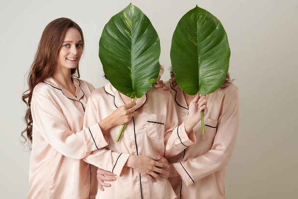 Giovani donne che coprono il viso dell'un l'altro con grandi foglie lussureggianti, cosmetici organici, concetto - Foto, immagini