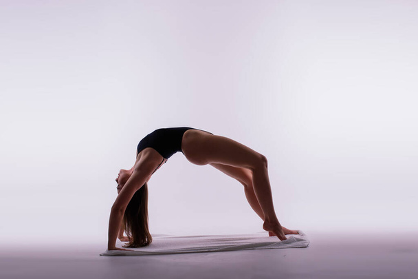 Athletic woman in a swimsuit doing yoga, plank pose variation, beautiful female exercising studio - Photo, Image