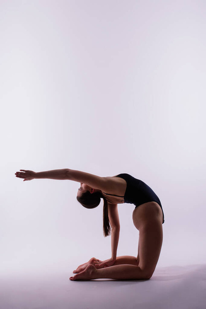 Athletic woman in a swimsuit doing yoga, plank pose variation, beautiful female exercising studio - Photo, Image