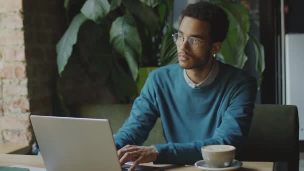 Mediana toma de joven empresario trabajando en el ordenador portátil en la mesa en coffeeshop - Imágenes, Vídeo