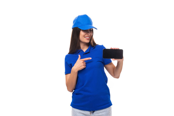 vrij vriendelijke jonge promotor vrouw in blauw katoen t-shirt en pet tonen smartphone mockup. - Foto, afbeelding