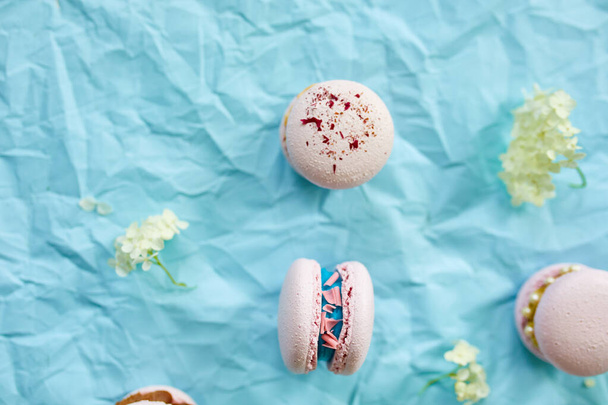 Macarons rosa dolce assortiti su sfondo blu con fiori freschi, assortimento di pasticceria, dolce indulgenza. - Foto, immagini