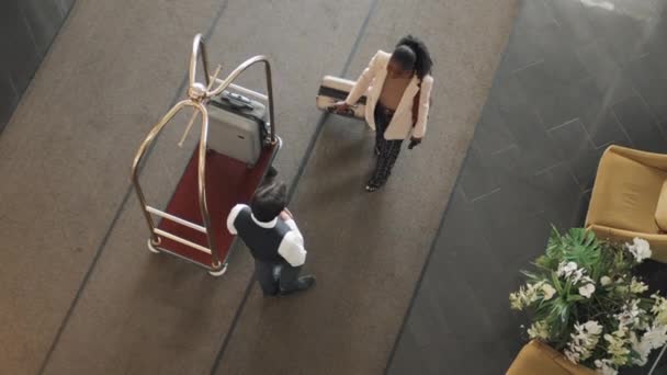 Зверху дзвіниця в уніформі, що працює в розкішному готелі, приймає нові гості валізи і перевозить їх за допомогою багажного візка - Кадри, відео