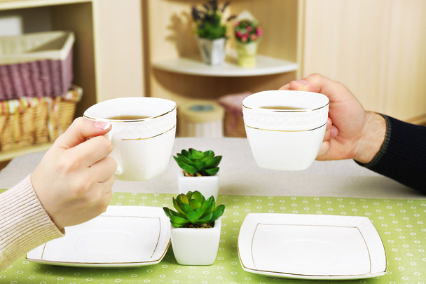 Female and male hands with cups of tea, close-up, on home interior background - Foto, immagini