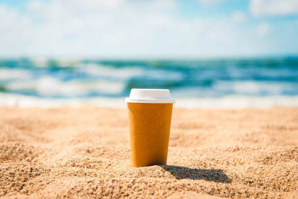 паперова чашка кави, чай стоїть у теплому піску. На тлі прекрасного моря і похмурого дня. Більш коричнева чашка кави на піщаному пляжі над хмарним небом і морем. - Фото, зображення
