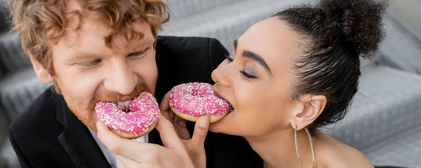 elegant interracial couple feeding each other with sweet donuts, wedding on street, fun, banner - Fotoğraf, Görsel