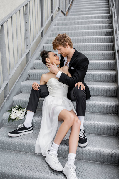 miejski romans, miłość, ślub na świeżym powietrzu, młoda para międzyrasowa obejmująca bliskie kwiaty na schodach - Zdjęcie, obraz