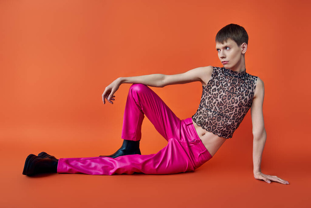 nonbinary person in leopard print sleeveless top and pink pants on orange backdrop, queer fashion - Fotó, kép