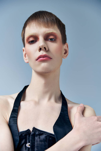 portrait, queer model with makeup looking at camera, posing on grey, beauty and visage, androgynous - Photo, Image