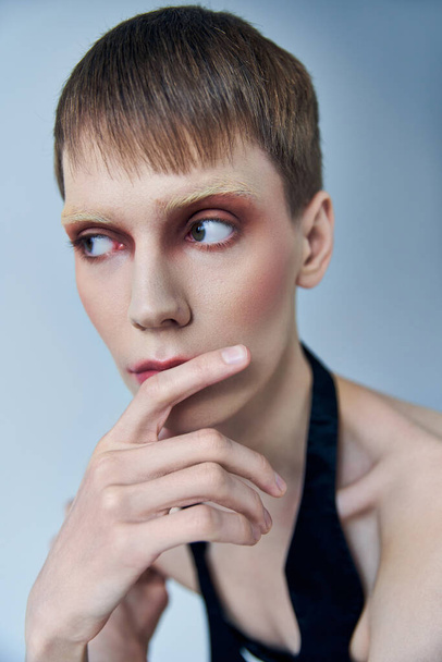queer model with makeup looking away on grey backdrop, androgynous person, portrait, identity - Фото, зображення