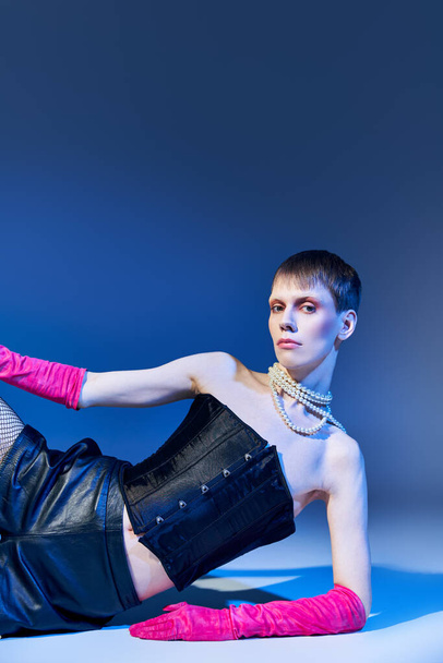 queer model in vet outfit en roze handschoenen poseren op blauwe achtergrond, shorts, niet-binaire, stijl - Foto, afbeelding