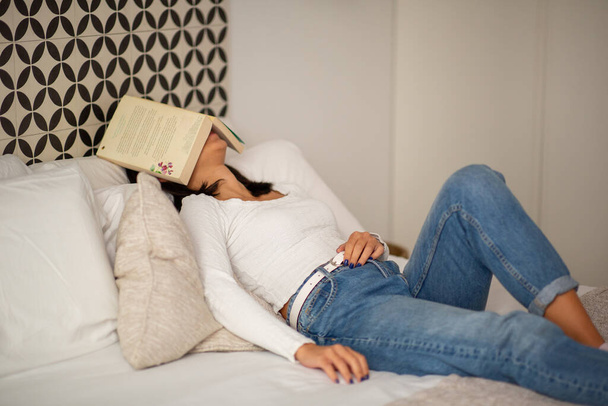 Portrait young woman sleeping in bed with book covering face - Photo, Image