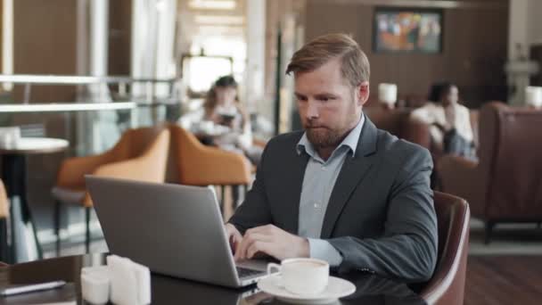 Σύγχρονη Καυκάσιος επιχειρηματίας κάθεται στο τραπέζι στο εστιατόριο του ξενοδοχείου που εργάζονται σε φορητό υπολογιστή χρησιμοποιώντας το Διαδίκτυο - Πλάνα, βίντεο