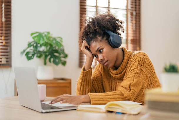 疲れたカーリーなアフリカ系アメリカ人の女性は,ラップトップの悲しみと距離の学習やオンライン教育についてイライラして自宅の机に座っています. - 写真・画像