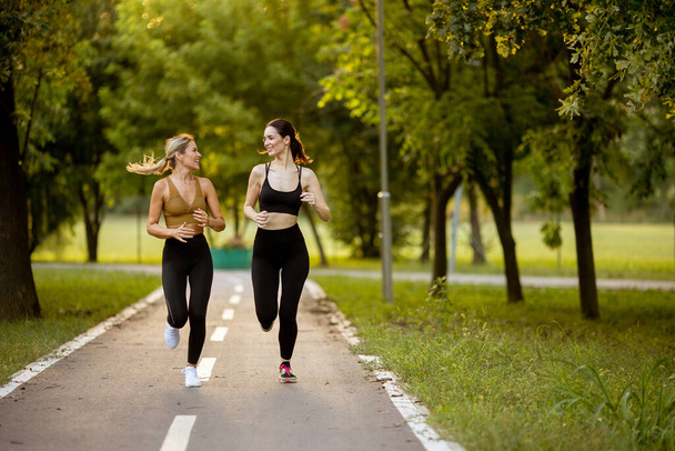 Zwei hübsche junge Frauen laufen auf einer Spur im Park - Foto, Bild