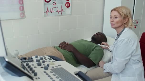 Tiro de ángulo alto de un joven negro con hipotiroidismo que se somete a examen por ultrasonografía - Imágenes, Vídeo