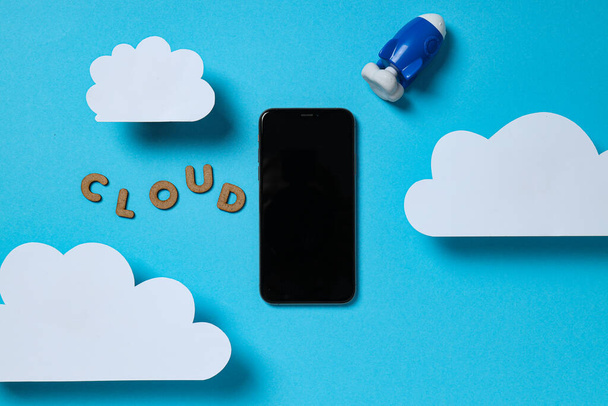 Fehér papír felhők egy játék rakéta, a szó "felhő" és egy okostelefon a kék háttér - Fotó, kép