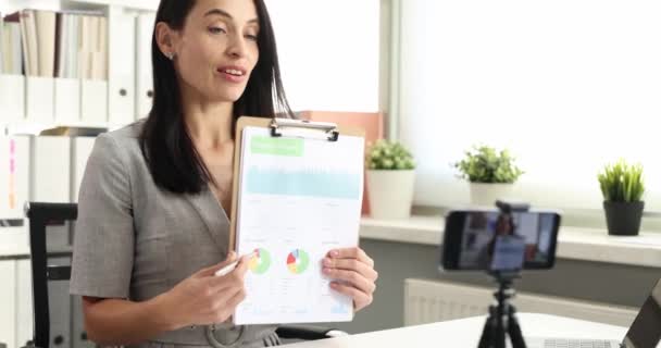Businesswoman holds financial report in charts and shows camera. Distance learning and online business conferences concept - Footage, Video