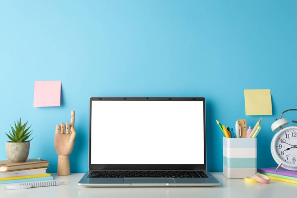 Maximieren Sie Ihre Remote Learning Messaging mit einer Seitenansicht-Komposition mit weißem Schreibtisch, Laptop, Uhr und Schreibwaren auf isoliertem blauem Hintergrund, bereit für Text- oder Werbeplatzierungen - Foto, Bild