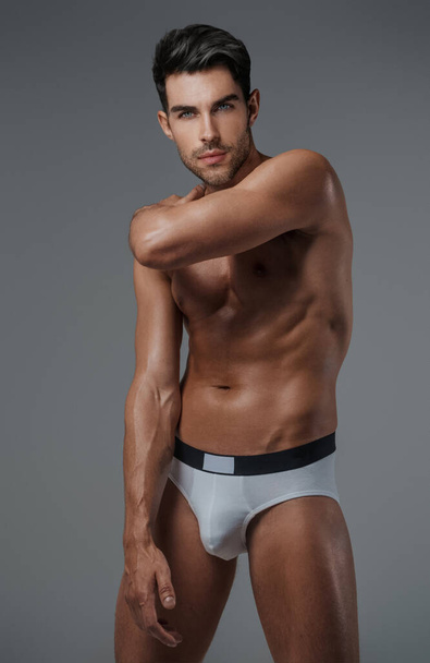 Сексуальная и харизматичная брюнетка мужского пола с голым туловищем и нижним бельем, на сером фоне - Фото, изображение