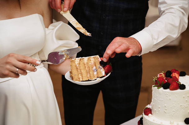 novia y novio cortar un pastel de bodas festivo en pedazos con un cuchillo - Foto, Imagen