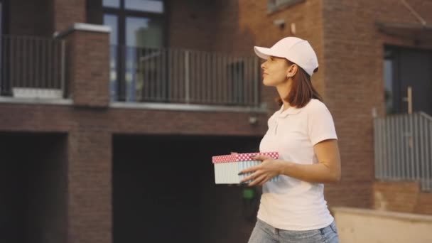 Beautiful Caucasian Lady Courier Going Along the Building Holding the Paper Surprise Boxes. Deliver Woman Worker. Market, Goods Delivery. Postwoman Gift Delivery for the Client. Delivering Postal - Footage, Video