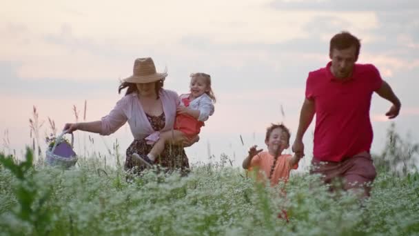 Щаслива кавказька сім'я біжить в руці через поле на заході сонця. Поняття щастя дитячих посмішок, спосіб життя сім'ї, відносини батьків з сином і дочкою.  - Кадри, відео