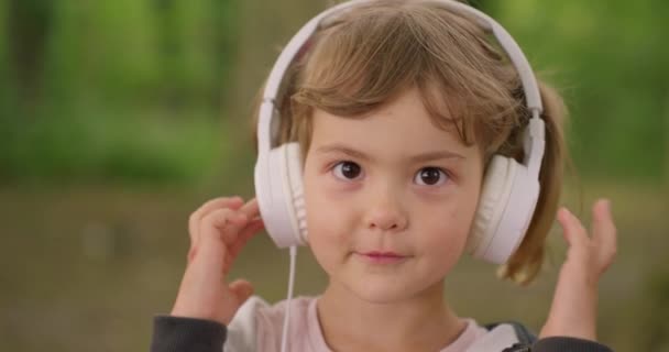 Egy kis aranyos lány nagy fejhallgatóval a szabadban. - Felvétel, videó