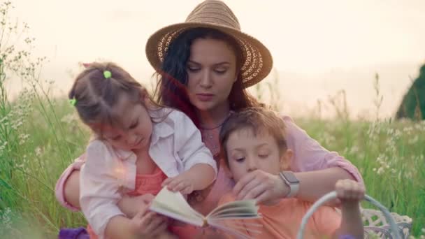 Momentos alegres: mamãe envolve crianças com um livro de histórias ao ar livre - Construindo fortes conexões familiares. Imagens 4k de alta qualidade - Filmagem, Vídeo