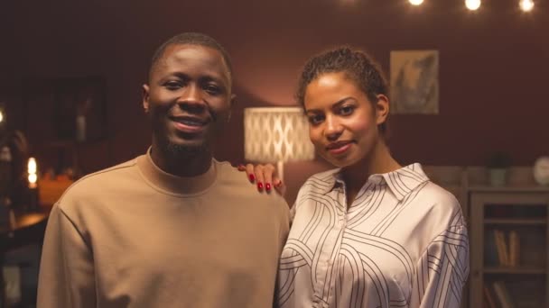 Ritratto medio di giovane felice coppia afroamericana in posa per la fotocamera in piedi in scuro elegante appartamento con lampadine - Filmati, video