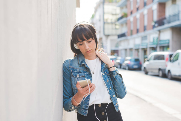 若い女性ミレニアル世代は,屋外でスマートフォンを使用して音楽を聞く - 写真・画像