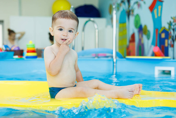 Fejlesztés csecsemőknek. Egy kisfiú megtanul úszni a medencében. A gyerekek első úszás leckéi. A csecsemők fejlődése - Fotó, kép