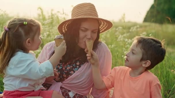 Ευτυχισμένη μαμά και παιδιά που απολαμβάνουν το παγωτό σε ένα ήρεμο πικνίκ στο πάρκο, ενσαρκώνοντας την έννοια της χαρούμενης παιδικής ηλικίας, ακτινοβολώντας χαμόγελα οικογενειακής ευτυχίας. Υψηλής ποιότητας 4k πλάνα - Πλάνα, βίντεο
