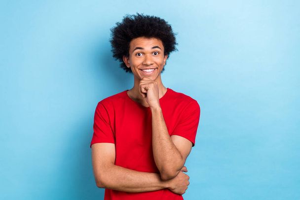 Portrait of optimistic intelligent person with chevelure hairdo wear red t-shirt hold fist on chin isolated on blue color background. - 写真・画像