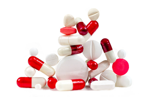 Rote und weiße Kapseln und Tabletten gestapelt auf weißem Hintergrund. - Foto, Bild