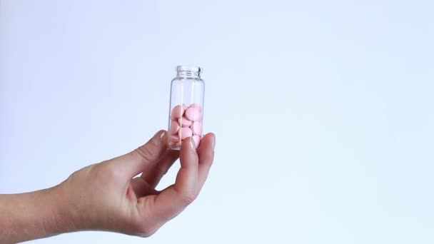 Vaaleanpunaisia pillereitä lasipullossa. Vitamiinit naisen kädessä valkoisella taustalla. Vitamiinit ja ravintolisät lähikuva - Materiaali, video
