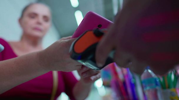 Kobieta płacąca rachunki przez smartfona z wykorzystaniem technologii NFC w supermarkecie. klient płaci za pomocą telefonu komórkowego przy użyciu technologii bezdotykowej. Zbliżenie rąk do płatności mobilnych - Zdjęcie, obraz