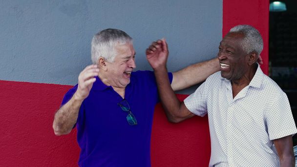 Authentic Interaction of Two Happy Diverse Older Friends, Hugging and Celebrating with High-Five, Standing Outside on Sidewalk. Joyeux compagnonnage entre les Afro-Américains et les Caucasiens - Photo, image