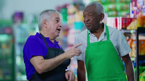 Ältere Mitarbeiter eines Lebensmittelgeschäfts diskutieren in Uniform über die Geschäftsführung im Gang des Supermarktes - Foto, Bild