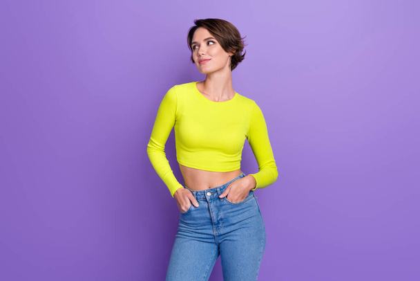 Photo of stunning minded lady put hands pockets look interested empty space wear lime top isolated on violet color background. - Foto, Imagem