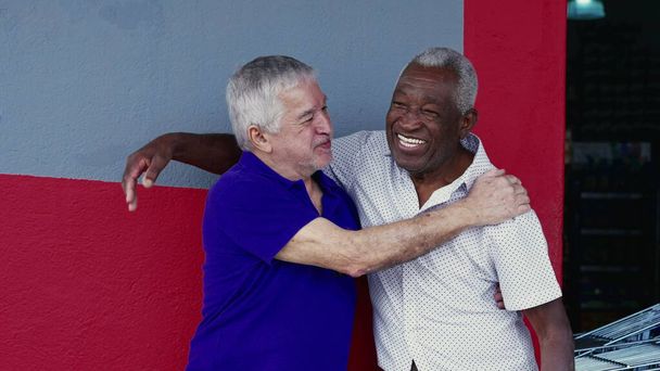Authentische Interaktion zweier glücklicher älterer Freunde, die sich umarmen und mit High-Five feiern, draußen auf dem Gehweg stehen. Fröhliche Kameradschaft zwischen Afroamerikanern und Kaukasiern - Foto, Bild