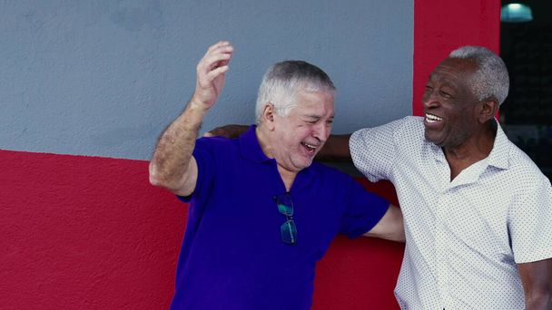Authentic Interaction of Two Happy Diverse Older Friends, Hugging and Celebrating with High-Five, Standing Outside on Sidewalk (em inglês). Companheirismo alegre entre indivíduos afro-americanos e caucasianos - Foto, Imagem