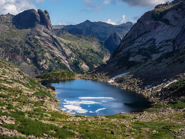 Дивовижний альпійський пейзаж з гірським озером у кам'яно-зеленій долині під блакитним небом. Атмосферні високогірні пейзажі з красивим льодовиковим озером серед сонячних пагорбів та скель на гірському хребті. - Фото, зображення