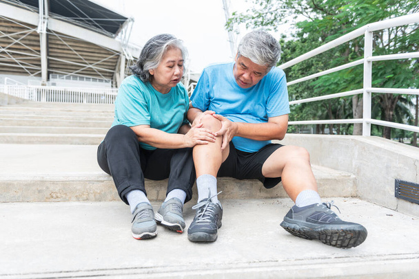 Ασιατικό ηλικιωμένο ζευγάρι, η σύζυγος αγγίζει και κοιτάζει το γόνατο του άντρα της, που είναι τραυματισμοί από την άσκηση. σε άτομα ηλικίας συνταξιοδότησης και την έννοια της οστεοαρθρίτιδας. - Φωτογραφία, εικόνα