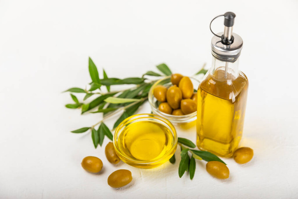 Olivenöl in einer Flasche und Soße auf dem Küchentisch. Ölflasche mit Zweigen und Früchten von Oliven. Platz für Text. Kopierraum. Pflanzenöl und Salatdressing. - Foto, Bild